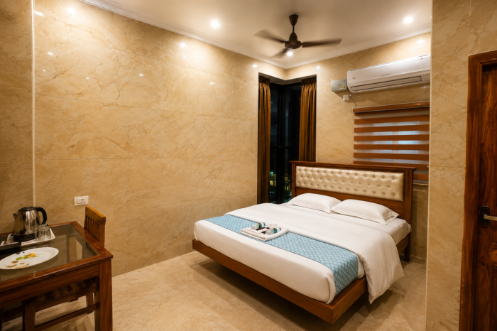 Premium Deluxe Queen Room at SSK Marina Residency featuring a comfortable queen-size bed with crisp white linens, elegant marble-finish walls, warm ambient lighting, air conditioning, flat-screen TV, work desk with tea and coffee facilities, modern wooden furnishings, and a clean, spacious interior designed for a relaxing and comfortable stay in Ramanathapuram.